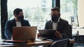 Business meeting during COVID-19 pandemic. Two young male Caucasian partners talk at modern office in face masks.