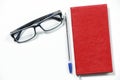 Black glasses, pen and red book isolated on a white table. Royalty Free Stock Photo