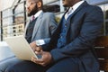 Business meeting of friends outdoors. Two dark-skinned men in suits are sitting on a bench near a city building with a Royalty Free Stock Photo