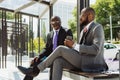 Business meeting of friends outdoors. Two dark-skinned men in suits are sitting on a bench near a city building with a Royalty Free Stock Photo