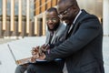 Business meeting of friends outdoors. Two dark-skinned men in suits are sitting on a bench near a city building with a Royalty Free Stock Photo