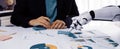 Business Meeting With Human and Robot Collaborating on Data Analysis with Charts and Graphs in Modern Office Environment Royalty Free Stock Photo