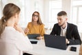 Business man with laptop thoughtfully looking aside while business woman in eyeglasses with folder in hand talking with