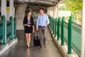 Businessman and businesswoman talk and walk together with black luggage on the public street, business travel