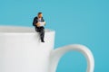 Business miniature figures sitting and read a book, read newspaper, waiting, talking and relax on white cup of hot coffee Royalty Free Stock Photo