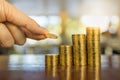 Business, Money, Finance and Saving Concept. Close up of man hand holding and put a coin to stack of coins on wooden table Royalty Free Stock Photo