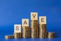 Business, Money and Saving Concept. Closeup of Englisg letter wooden block on top of stack of gold coins on blue background