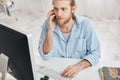 Business, office and technology concept. Top view of bearded employee wearing blue shirt, talking on phone with