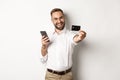 Business and online payment. Excited man showing his credit card while holding smartphone, standing satisfied against Royalty Free Stock Photo