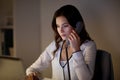 Woman with laptop calling on phone at night office