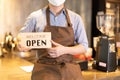 Business owner attractive young Asian man in apron hanging we`re open sign on front door  welcoming clients to new cafe. Happy Royalty Free Stock Photo