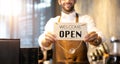 Business owner attractive young Asian man in apron hanging we`re open sign on front door  welcoming clients to new cafe. Happy Royalty Free Stock Photo