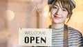 Business owner attractive young Asian woman in apron hanging we`re open sign on front door smiling welcoming clients to new cafe. Royalty Free Stock Photo