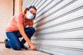 A business owner closes her business definitively by lowering the metal blind due to the economic crisis