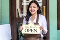 Young asian woman in apron looking at camera, we& x27;re open sign on front door smiling welcoming Royalty Free Stock Photo