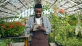 Business owner walking in greenhouse writing in notebook doing inventory smiling