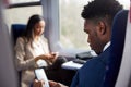 Business Passengers Sitting In Train Commuting To Work Looking At Mobile Phones