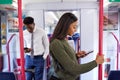 Business Passengers Standing In Train Commuting To Work Looking At Mobile Phones