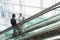 Business people with bags talking with each other on escalator in a modern office Royalty Free Stock Photo