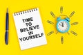On a yellow surface there is an alarm clock, a pen and a notepad with the inscription - Time to Believe in Yourself Royalty Free Stock Photo