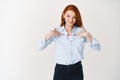 Business people. Confident redhead woman pointing at herself, you need me gesture, asking for job, standing in blue Royalty Free Stock Photo