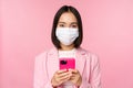 Business people and covid-19 concept. Japanese corporate office lady in suit and medical face mask, using mobile phone Royalty Free Stock Photo