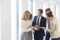 Business people discussing over document while standing in corridor at office Royalty Free Stock Photo
