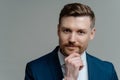 Handsome thoughtful entrepreneur thinking about business and looking at camera while standing against grey background Royalty Free Stock Photo