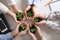 Business people holding green seedlings with soil on light table, top view Royalty Free Stock Photo