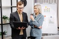 Business people with laptop discussing new projects in office. A young woman and a man stand near flipcharts and solve work issues Royalty Free Stock Photo