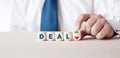 Business person is turning a wooden cube with the arrows next to the word deal. The decision or dilemma to accept or reject a