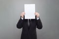 Business person wearing black suit hiding his face behind blank empty white paper on gray studio wall background Royalty Free Stock Photo