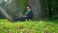 Business person working on laptop, sitting under tree, escaping busy lifestyle Royalty Free Stock Photo