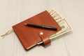 A brown leather notebook and black pen lie on an office desk. Cash dollars. Royalty Free Stock Photo