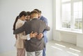 Group of business people standing in a close circle in a bright empty room and hugging each other.