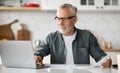 Business After Retirement. Smiling Senior Man Working With Laptop In Kitchen Interior Royalty Free Stock Photo