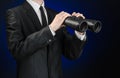Business and search topic: Man in black suit holding a black binoculars in hand on a dark blue background in studio isolated Royalty Free Stock Photo