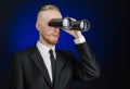 Business and search topic: Man in black suit holding a black binoculars in hand on a dark blue background in studio isolated Royalty Free Stock Photo