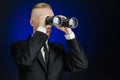 Business and search topic: Man in black suit holding a black binoculars in hand on a dark blue background in studio isolated Royalty Free Stock Photo