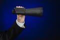 Business and search topic: Man in black suit holding a black binoculars in hand on a dark blue background in studio isolated Royalty Free Stock Photo