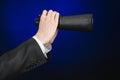 Business and search topic: Man in black suit holding a black binoculars in hand on a dark blue background in studio isolated Royalty Free Stock Photo