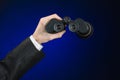 Business and search topic: Man in black suit holding a black binoculars in hand on a dark blue background in studio isolated Royalty Free Stock Photo