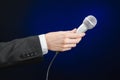 Business and speech topic: Man in black suit holding a microphone on a gray dark blue isolated background in studio Royalty Free Stock Photo