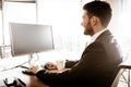 Business succsess concept. Happy smiling young businessman back sitting in office and working on computer. Man in suit Royalty Free Stock Photo