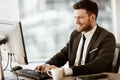 Business succsess concept. Happy smiling young businessman sitting in office and working on computer. Man in suit Royalty Free Stock Photo