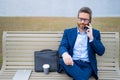 Business talk. Businessman talk on phone sitting on a bench in park. Businessman in suit call phone outside. Businessman Royalty Free Stock Photo