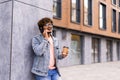 Business talk on a go. Confident young man in glasses holding coffee cup and talking on mobile phone while walking outdoors Royalty Free Stock Photo