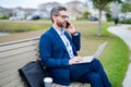 Business talk. Business man talk on phone sitting on a bench in park. Man in suit call phone outside. Handsome business Royalty Free Stock Photo