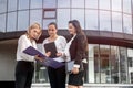 Business team. Three women in suits with folders and tablet posing outside building