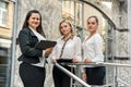 Business team. Three women in suits with folders and tablet posing outside building